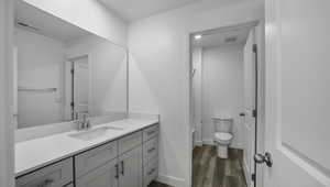 Full bath with baseboards, visible vents, toilet, wood finished floors, and vanity