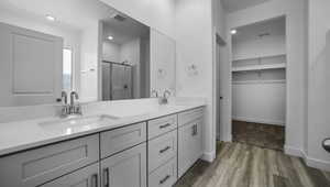 Bathroom with double vanity, visible vents, a sink, a shower stall, and wood finished floors