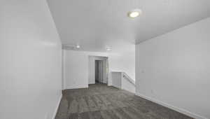 Empty room featuring a textured ceiling, carpet flooring, and baseboards