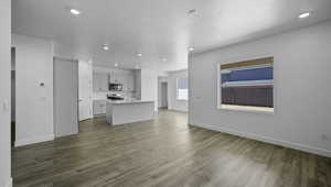 Unfurnished living room with a textured ceiling, wood finished floors, and baseboards