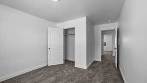 Unfurnished bedroom with a textured ceiling, baseboards, dark colored carpet, and a closet