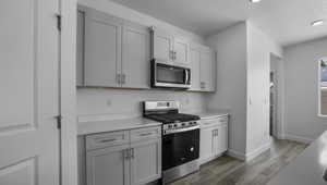 Kitchen featuring baseboards, appliances with stainless steel finishes, wood finished floors, light countertops, and a textured ceiling