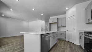 Kitchen with electric stove, dishwasher, wood finished floors, light countertops, and a sink