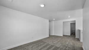 Empty room with carpet, a textured ceiling, and baseboards