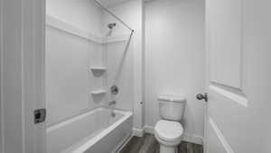 Bathroom with shower / bath combination, baseboards, toilet, and wood finished floors