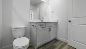 Half bathroom featuring baseboards, vanity, toilet, and wood finished floors