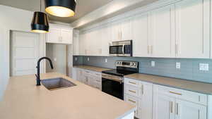 Kitchen featuring decorative backsplash, decorative light fixtures, stainless steel appliances, white cabinetry, and a sink