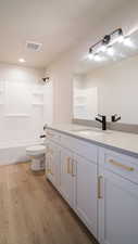 Full bath with visible vents, toilet, wood finished floors, tub / shower combination, and vanity