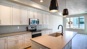 Kitchen featuring an island with sink, a sink, stainless steel appliances, light wood-type flooring, and backsplash