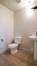 Half bath with toilet, wood finished floors, visible vents, and baseboards