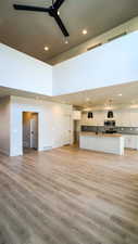 Unfurnished living room with ceiling fan, a towering ceiling, light wood-style flooring, and recessed lighting