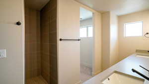 Full bath with a tile shower, double vanity, a sink, and baseboards