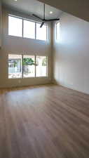 Unfurnished living room featuring baseboards, ceiling fan, wood finished floors, a high ceiling, and recessed lighting