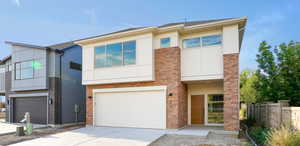 View of front of home featuring a garage, brick siding, fence, concrete driveway, and stucco siding