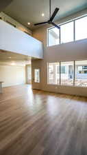 Unfurnished living room with a towering ceiling, wood finished floors, a ceiling fan, and baseboards