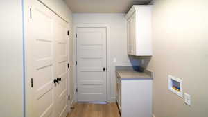 Laundry room featuring light wood finished floors, washer hookup, and cabinet space