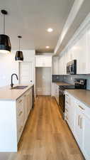 Kitchen featuring light wood finished floors, appliances with stainless steel finishes, white cabinetry, a sink, and an island with sink