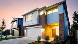 View of front of property with brick siding, driveway, an attached garage, and stucco siding