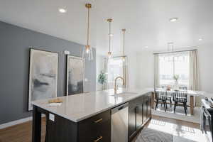 Kitchen with light stone counters, wood finished floors, a sink, baseboards, and appliances with stainless steel finishes