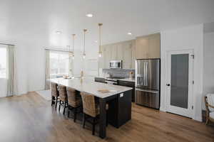 Kitchen with wood finished floors, appliances with stainless steel finishes, an island with sink, and a sink