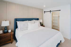 Bedroom with a barn door, a decorative wall, a walk in closet, and light colored carpet