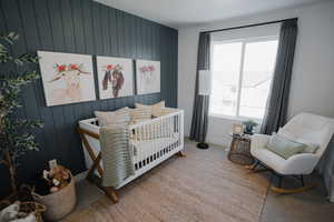 Bedroom featuring wooden walls, carpet, a crib, and baseboards