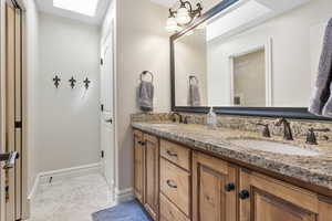 Bathroom featuring a skylight, a sink, baseboards, and double vanity
