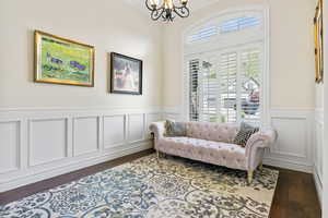 Living area with a decorative wall, dark wood-type flooring, ornamental molding, wainscoting, and a chandelier