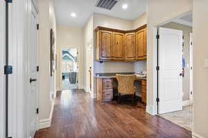 Office space featuring recessed lighting, visible vents, baseboards, built in study area, and dark wood-style floors