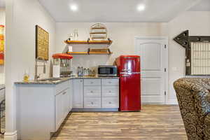 Kitchen with open shelves, stainless steel microwave, a sink, and light wood-style flooring