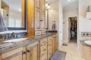 Bathroom with crown molding, a sink, a bath, and double vanity