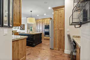 Kitchen featuring light wood finished floors, a center island, light stone countertops, stainless steel appliances, and recessed lighting