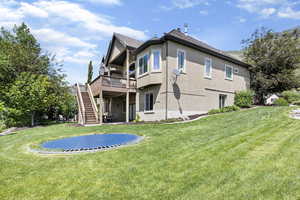Back of property featuring a yard, stairway, a wooden deck, and stucco siding