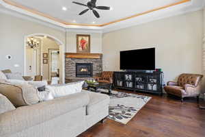 Living room featuring ceiling fan, wood-type flooring, a raised ceiling, and a stone fireplace