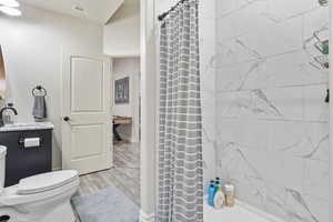 Full bathroom with toilet, wood finished floors, vanity, visible vents, and a shower with curtain