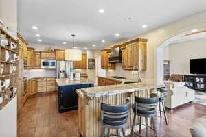 Kitchen featuring arched walkways, wood-type flooring, appliances with stainless steel finishes, a sink, and premium range hood