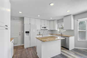 Kitchen with white appliances, a sink, white cabinets, light stone countertops, and dark wood finished floors