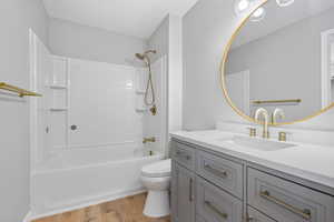 Bathroom with vanity, bathtub / shower combination, wood finished floors, and toilet