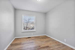 Empty room with baseboards, visible vents, and wood finished floors