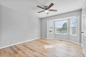 Empty room with visible vents, ceiling fan, light wood-style flooring, and baseboards