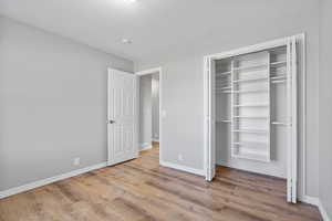 Unfurnished bedroom featuring a closet, a textured ceiling, baseboards, and wood finished floors