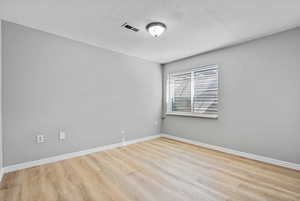 Unfurnished room with visible vents, a textured ceiling, baseboards, and wood finished floors