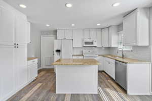 Kitchen with white appliances, a sink, white cabinets, light stone countertops, and dark wood finished floors