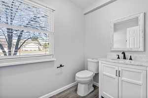 Half bathroom with vanity, wood finished floors, toilet, and baseboards