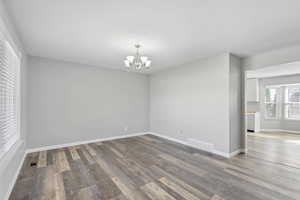 Empty room with baseboards, wood finished floors, visible vents, and a notable chandelier