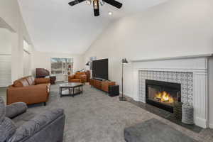 Living room featuring high vaulted ceiling, a fireplace, carpet flooring, baseboards, and ceiling fan