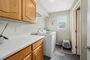 Laundry area featuring washing machine and clothes dryer, cabinet space, baseboards, and stone finish floor