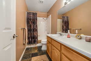 Bathroom featuring visible vents, toilet, stone tile floors, baseboards, and vanity