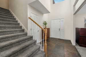 Foyer entrance with stone tile floors, stairway, baseboards, and a towering ceiling