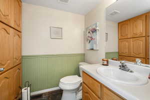 Half bathroom featuring a wainscoted wall, toilet, visible vents, and vanity